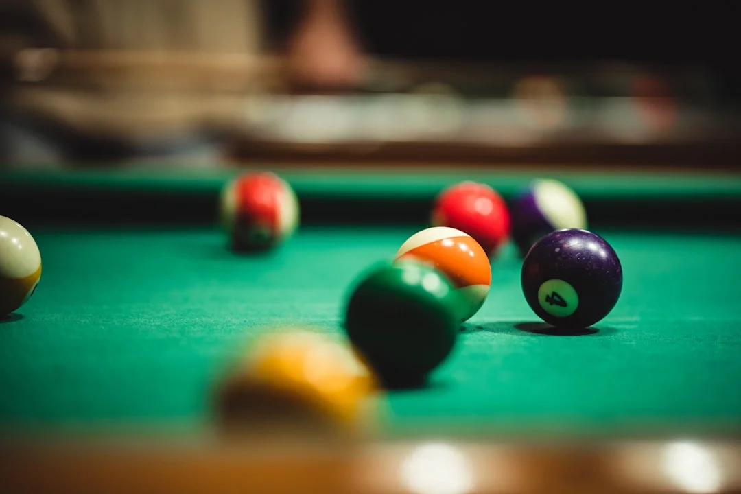 A warmly lit game room featuring a premium three-piece slate pool table with deep green felt, solid hardwood cabinetry, and a pendant billiard light overhead